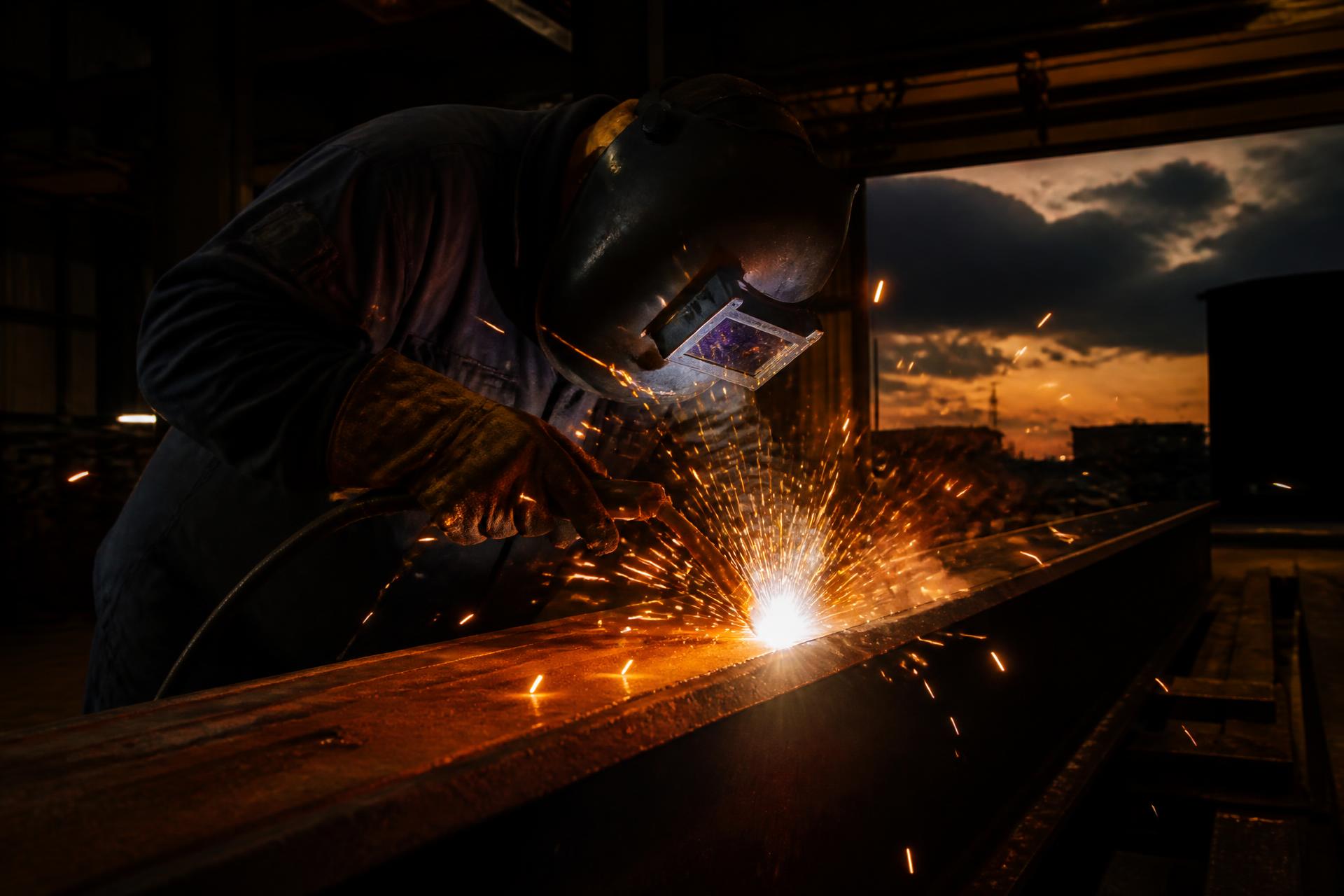 Welder fabricating a structural steel beam with sparks flying